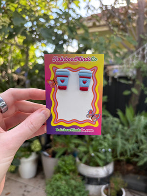 Hand holding a colorful card with a a coffee cup polymer clay earrings and 'RainbowMindsCo' branding, outdoors.